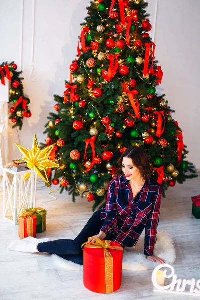 Chica sentada en un piso cerca de un árbol de navidad y un gran regalo un — Foto de Stock