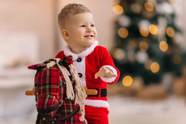 Primo piano del bambino in costume da Babbo Natale su cavallo a dondolo e sorriso. blu — Foto Stock