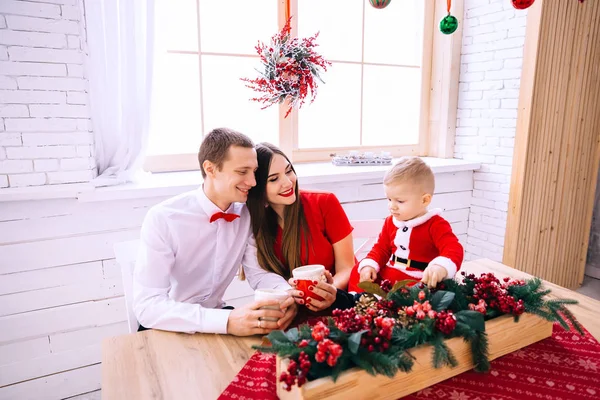 Kleine jongen zittend op een tafel in een kerstmanpak. ouders zitten een — Stockfoto