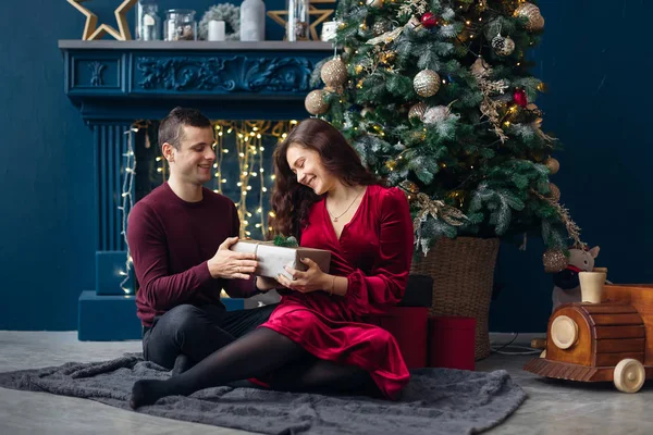 guy gives a gift to a girl. couple in love sitting near Christma