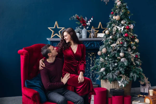 Casal sentado na poltrona vermelha perto da árvore de Natal e lareira — Fotografia de Stock