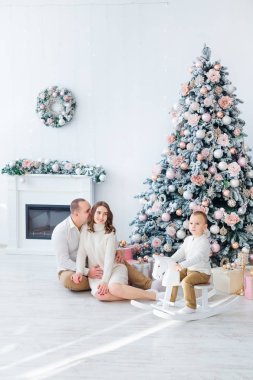 Annem ve babam Noel ağacı ve şöminenin yanında oturuyorlar. Çocuk oturur. 