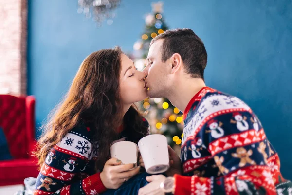 Ragazzo e ragazza baciare e tenere in mano tazza con bevanda calda. accogliente camera w — Foto Stock