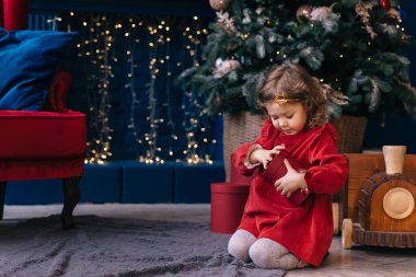 Elbiseli küçük kız Noel ağacının yanındaki hediye kutusunu açıyor. Armchai.