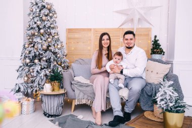 Ebeveynler bebeğe sarılıp kanepede oturuyorlar. Güzel bir Noel.