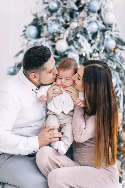 Mamma e papà abbracciare e baciare piccolo figlio vicino albero di Natale. — Foto Stock