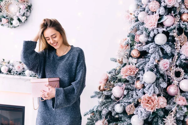 Ragazza in un maglione grigio tiene la mano nei capelli e tiene un regalo vicino — Foto Stock