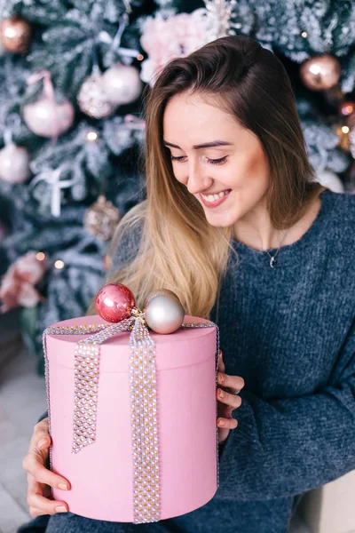 Χαριτωμένο κορίτσι κάθεται πάνω στο χριστουγεννιάτικο δέντρο και κρατώντας το κουτί — Φωτογραφία Αρχείου