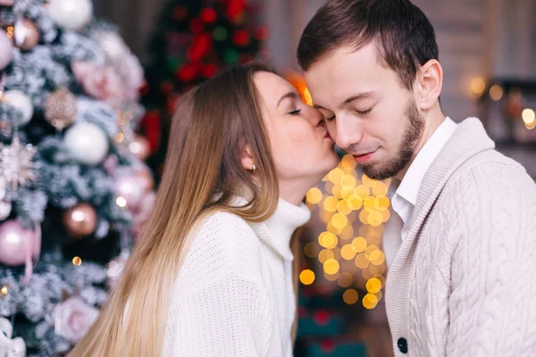 Ragazza bacia un ragazzo sulla guancia su uno sfondo di albero di Natale — Foto Stock