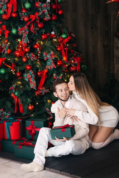 Couple assis près de l'arbre de Noël avec des cadeaux. le gars fermé salut — Photo