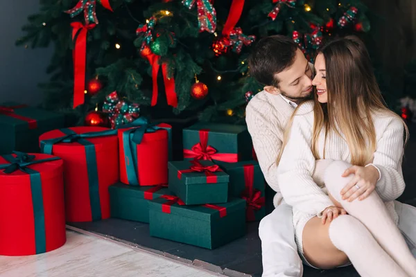 Coppia seduta vicino all'albero di Natale e regali in maglia bianca — Foto Stock