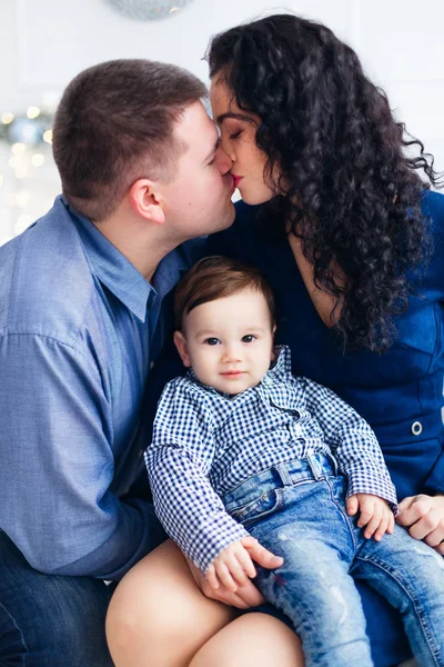 closeup of parents kissing and little son between them looking i