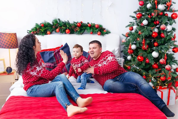 Anya, apa és kisfiú az ágyon a karácsonyfa mellett. Nézd a családot.. — Stock Fotó