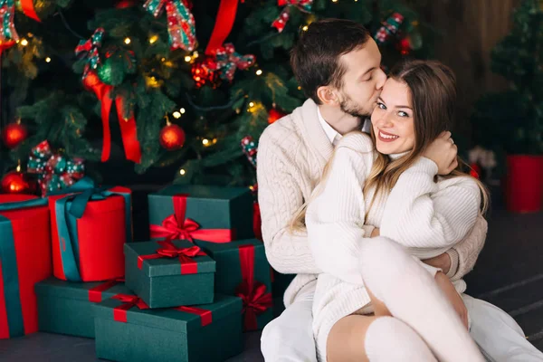 Coppia seduta vicino all'albero di Natale e regali in maglia bianca — Foto Stock