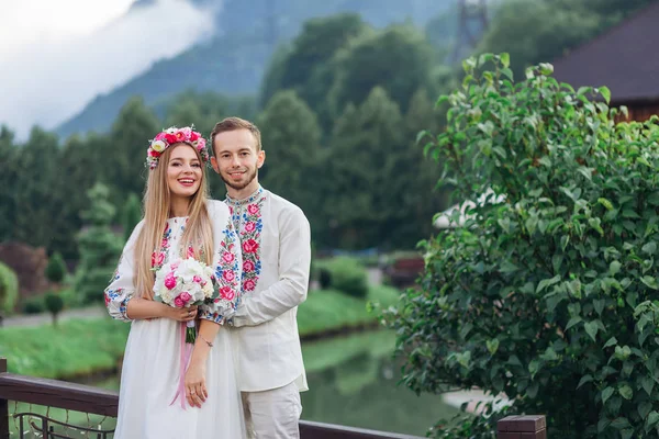 Recién casados en ropa bordada sonriendo y mirando el vino — Foto de Stock