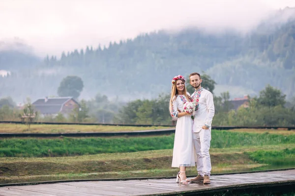 Recém-casados em roupas bordadas olhar para a câmera no fundo — Fotografia de Stock