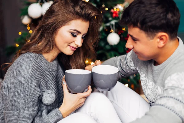 Bella ragazza e ragazzo seduto vicino a un albero di Natale e tenendo — Foto Stock