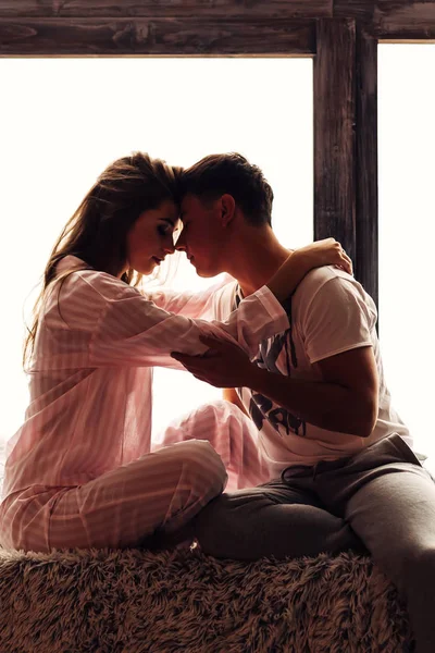 Verliebte Paare im Pyjama sitzen auf der Fensterbank und umarmen sich. — Stockfoto