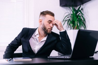 Bitkin hissediyorum. Hüsrana uğramış genç sakallı adam ofisteki iş yerinde otururken burnuna masaj yapıyor ve gözlerini kapalı tutuyor.