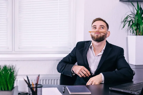 man takes a break from work. Millennial guy having fun making a mustache by applying a pencil under his nose