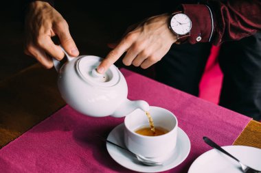 Adam çaydanlığı tutuyor ve fincana sıcak çay döküyor. Kafe. Erkek eli..