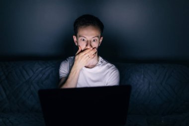 Bilgisayara bakan şaşkın adam şaşırmış ve elleriyle ağzını kapatmış.