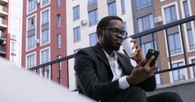 Genç Çekici İş Adamı akıllı telefonuna mesaj yazıyor ve kahve içiyor. Tatmin olmuş görünüyorsun. Klasik takım elbiseli sakallı adam. İş hayatı tarzı.