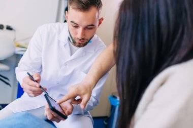 Diş hekimi ve hasta telefondaki diş hekiminin röntgen görüntüsü üzerinde birlikte bakarlar..