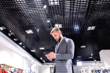 Genç adam elbise mağazasında akıllı telefon kullanıyor.