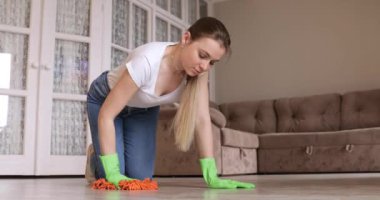 Diz çöküp yeşil koruyucu eldivenleriyle yerleri temizleyen genç bir kadın.