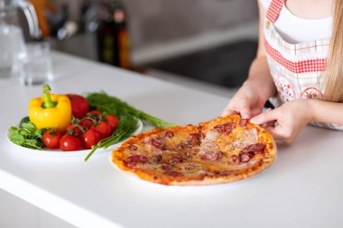 Kadın elleri pepperoni pizzasından bir dilim alıyor. 