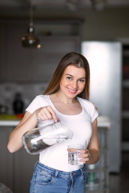 Mutlu genç ev hanımı bir sürahide filtrelenmiş su doldurur.