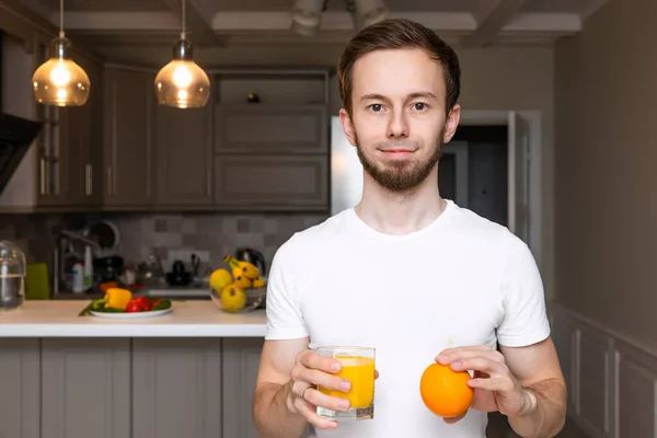 Portrait of a smiling young man with an orange and a glass of orange juice.