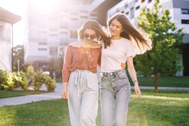 Üniversite arkadaşları kampüste yürüyor, konuşuyor, dersten sonra ara veriyorlar.