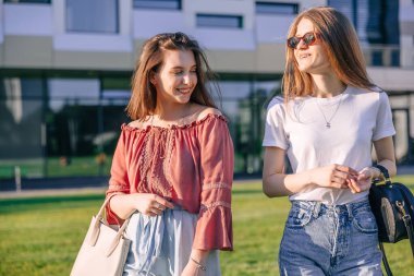 Güneşli bir günde modern bir şehirde iki çekici kız yürüyor. Mutlu gülümseyen kız arkadaşların portresi.