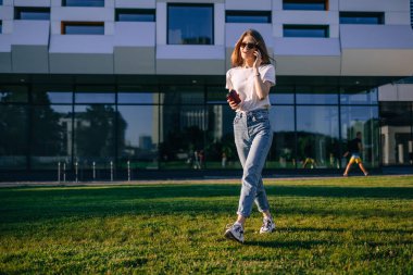 Genç bir kız evin yanında yürüyor, kahve içiyor, telefonda konuşuyor..