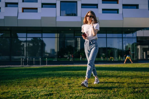 Genç bir kız evin yanında yürüyor, kahve içiyor, telefonda konuşuyor..