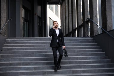 Takım elbiseli genç adam telefonda konuşuyor.
