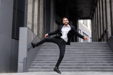 Resmi takım elbiseli mutlu genç adam merdivenlerde zıplıyor.