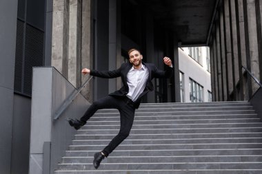 Resmi takım elbiseli mutlu genç adam merdivenlerde zıplıyor.