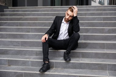 Resmi takım elbiseli çaresiz genç adam merdivenlerde oturuyor.