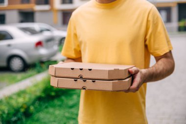Kurye, şehrin arka planında iki pizza kutusu tutuyor.