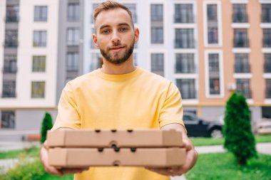 Sarı tişört giyen teslimatçı elinde iki paket pizza kutusu tutuyor. 