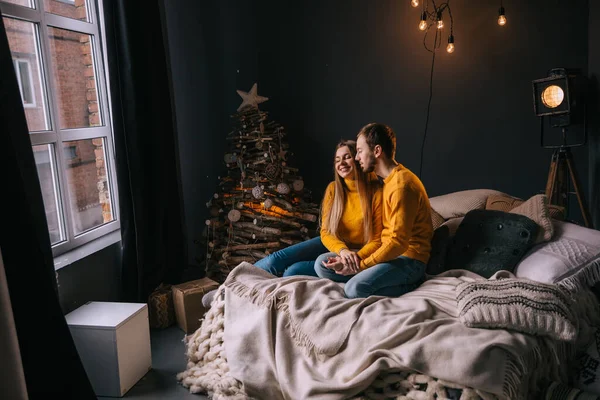 Happy couple in love lying in bed in the bedroom with a Christmas tree and gifts near the window. Cozy home moment. Christmas morning.