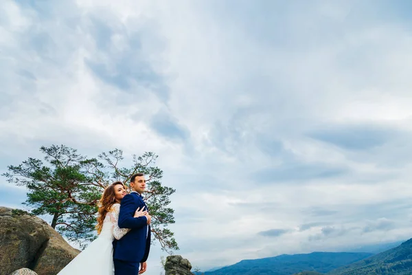 Noiva Abraça Noivo Lado Trás Contra Fundo Das Montanhas — Fotografia de Stock