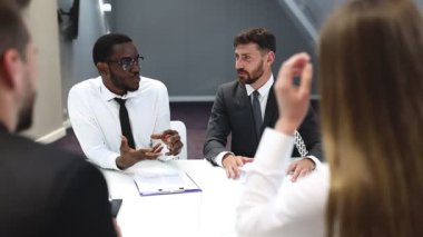 Takım elbiseli bir işadamı iş arkadaşlarıyla ya da ortaklarıyla konferans masasında oturuyor, erkek lider takım çalışmasını tartışıyor ya da müşterilerle grup görüşmeleri yapıyor.