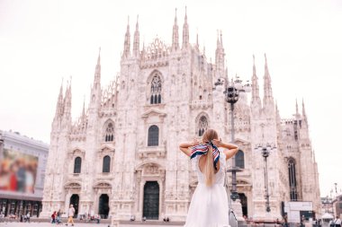 Beyaz elbiseli bir kızın arkadan görünüşü başörtüsünü düzeltir ve Duomo Katedrali 'ne bakar, Milano, İtalya.