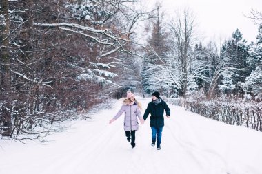 Mutlu çift kış ormanında eğleniyor. El ele tutuşup karla dolu çayırda koşuyorlar..