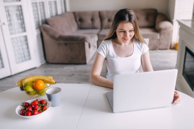 Modern dizüstü bilgisayar kullanan gülümseyen bir kız, bilgisayarında çalışan mutlu genç bir kadın, evden mesaj yazan, teknoloji konsepti