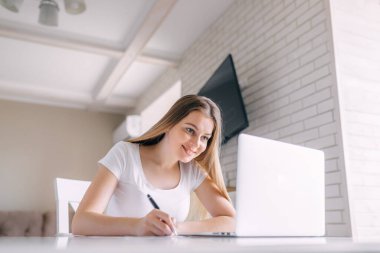 Bir kadın internette yeni bir teknik cihazdan video izliyor. Notlar yapar